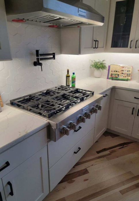 A stainless steel gas range with a pot filler faucet mounted on a hexagon tile backsplash in a modern kitchen in manhattan, KS.